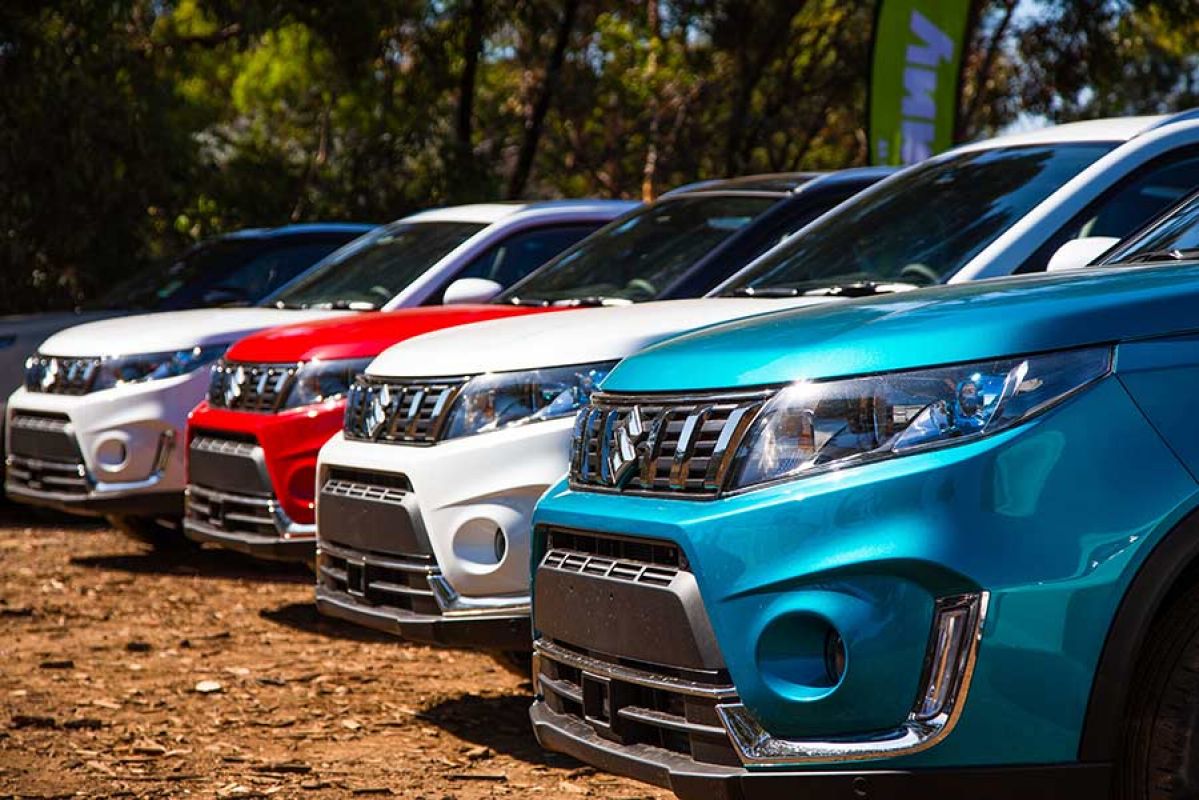 Front side view of the nose of a blue, two white and a red Suzuki Vitara Series II parked next to each other on a dirt road