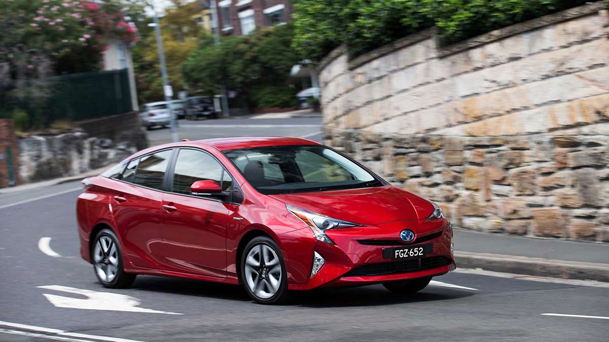 Front side view of a red Toyota Prius driving on a bendy road