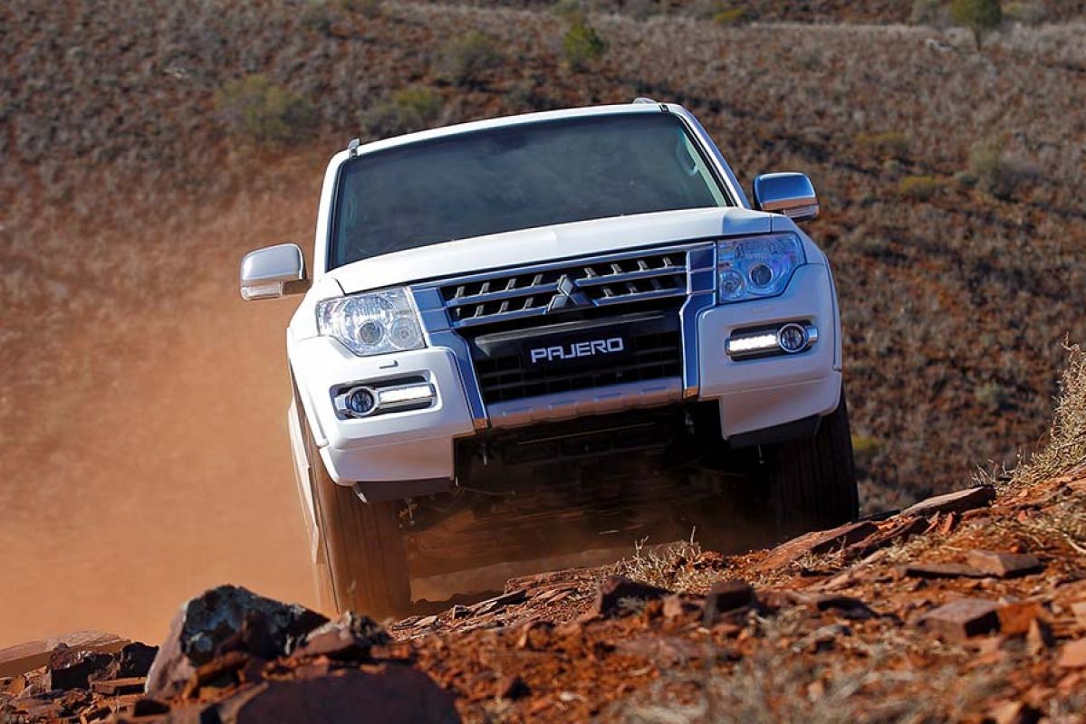 White Mitsubishi Pajero driving through rocky dunes