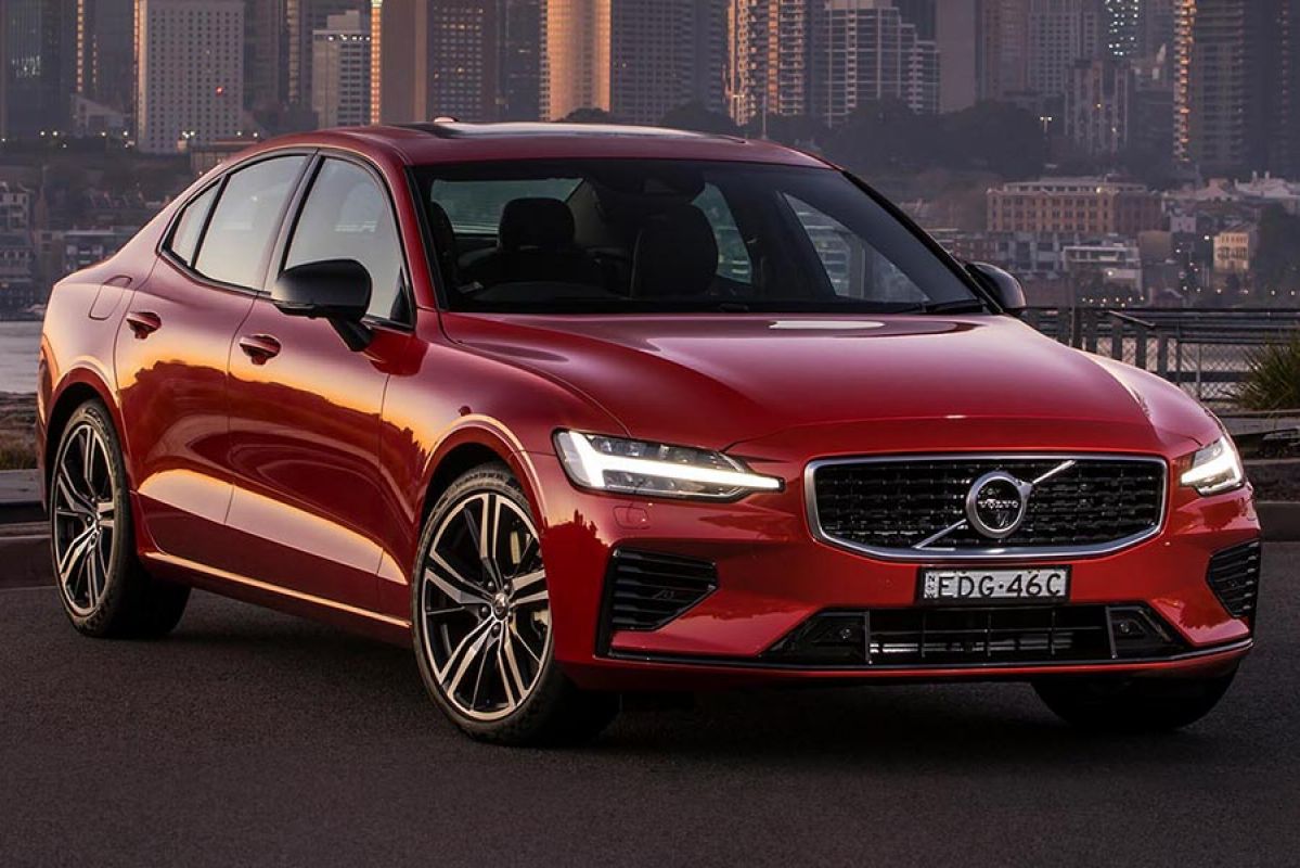 Front side view of a red Volvo S60 T8 R-Design 2020 car parked on tarmac with a river and a city skyline in the background