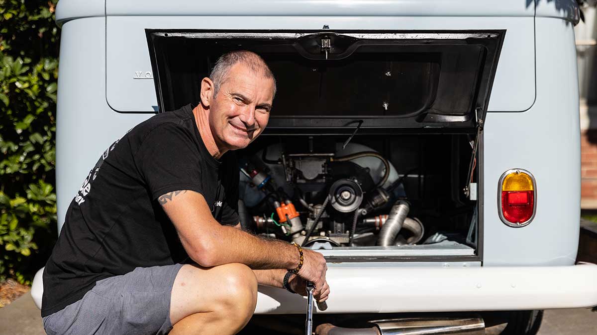 man kneeling next to the engine of a VW Kombi