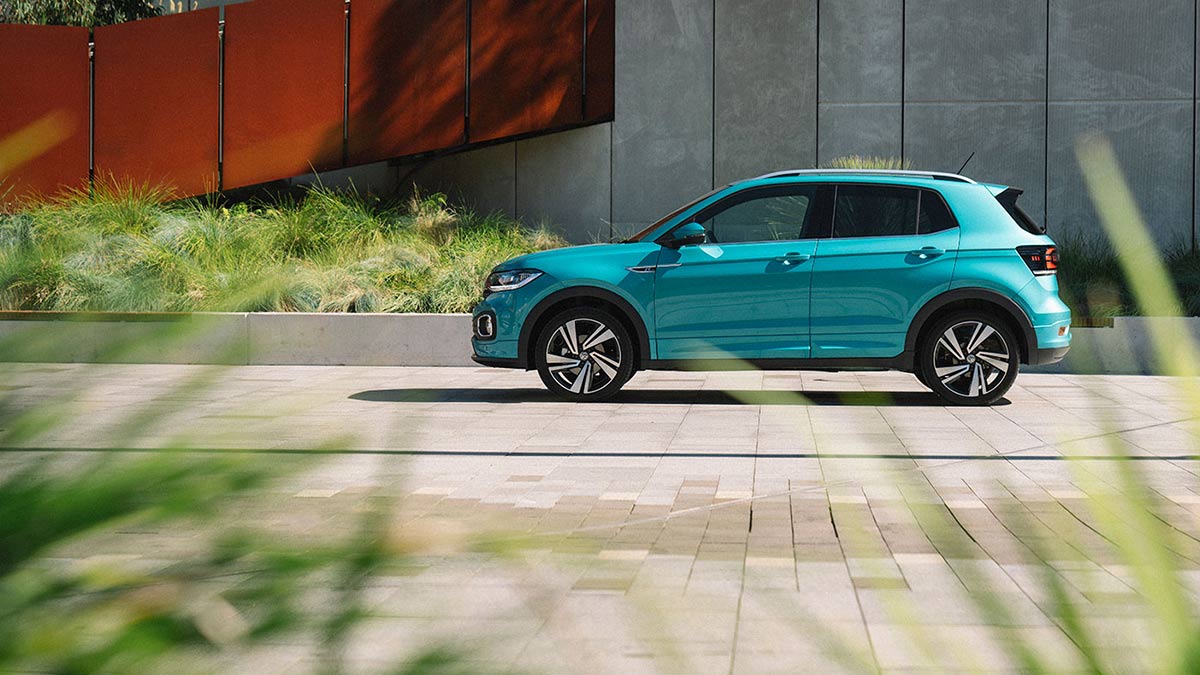 Side view of a turquoise Volkswagen T-Cross 85 TSI Style 2020 car parked in front of a building