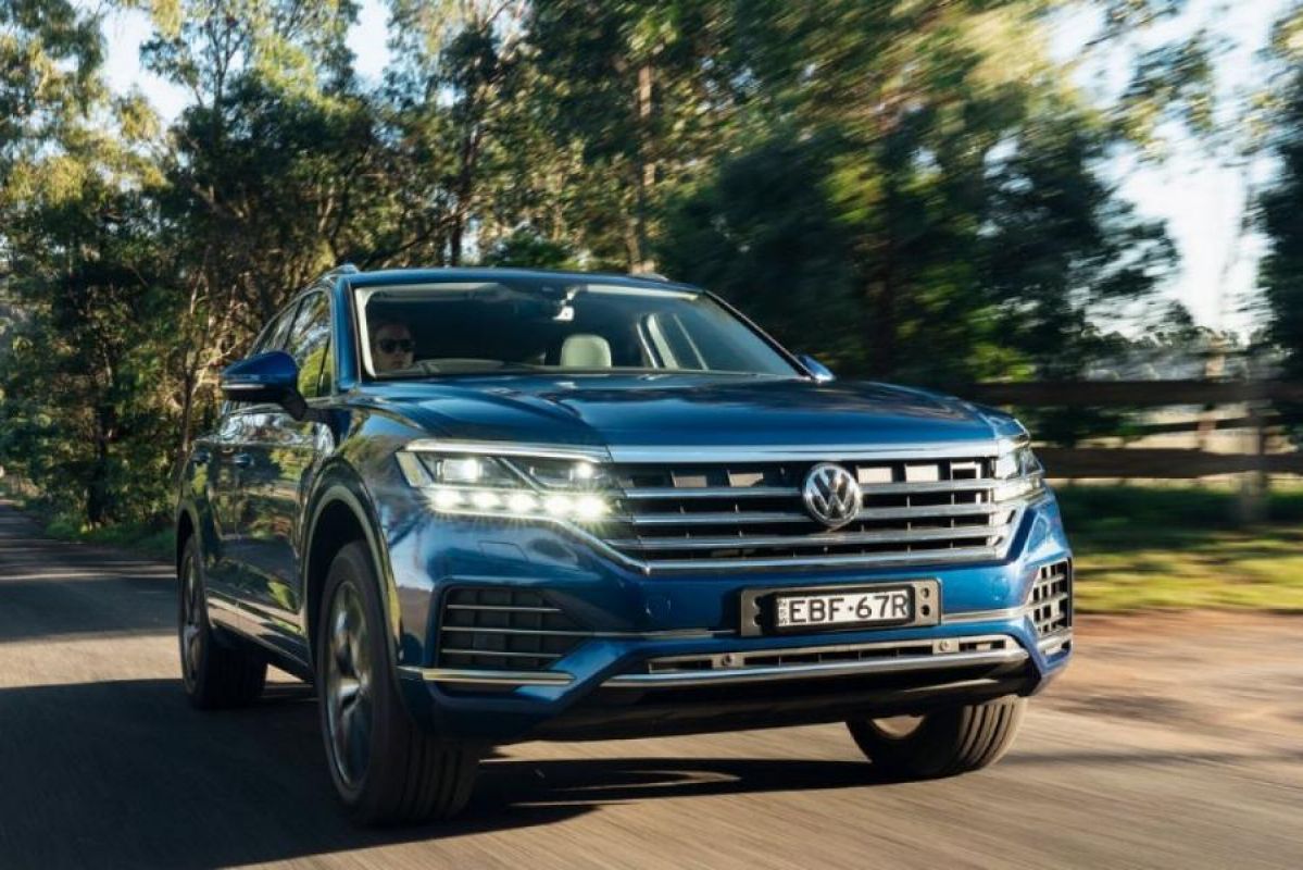 blue volkswagen touareg driving on country road next to trees