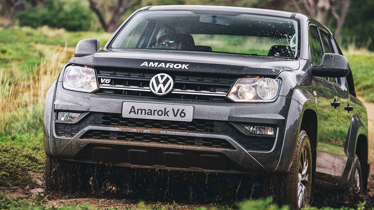 Front side angled view of a grey Volkswagen Amarok V6 driving up a muddy road in a green valley