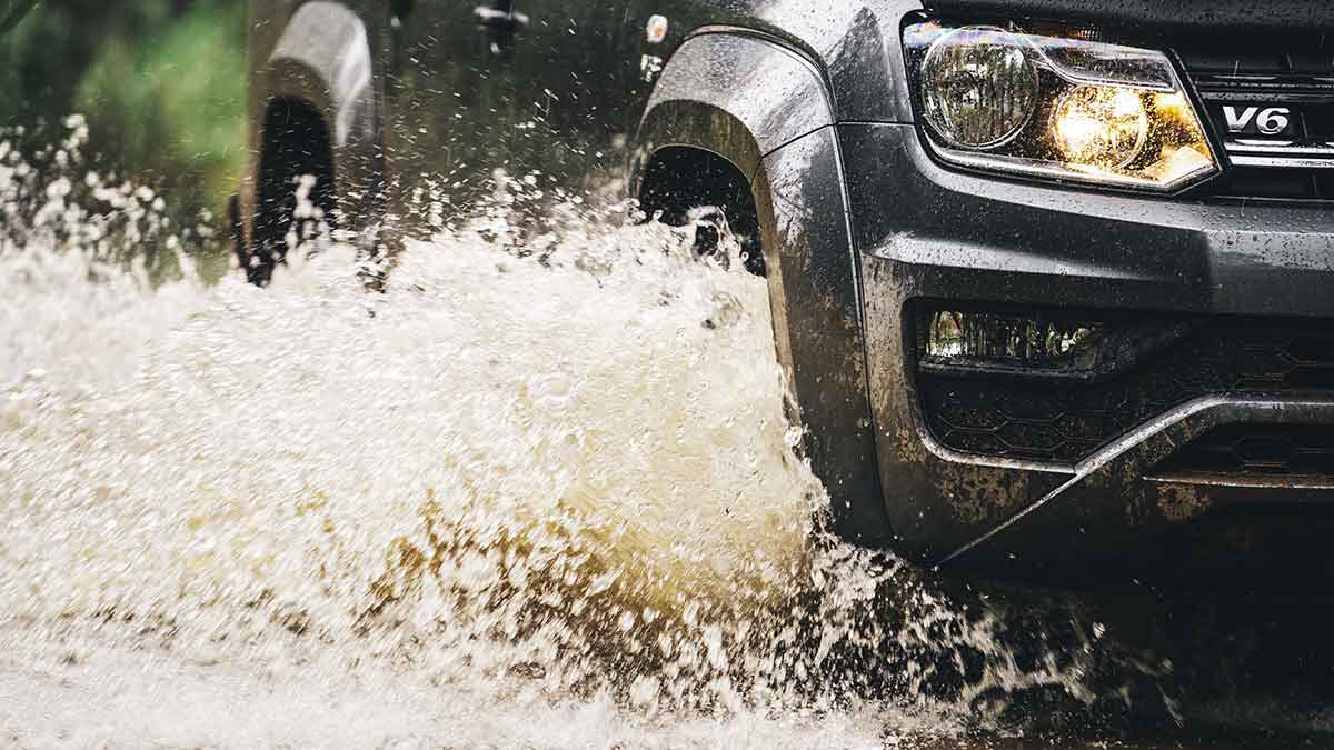 Front side view of a grey Volkswagen Amarok V6 as it drives through muddy water