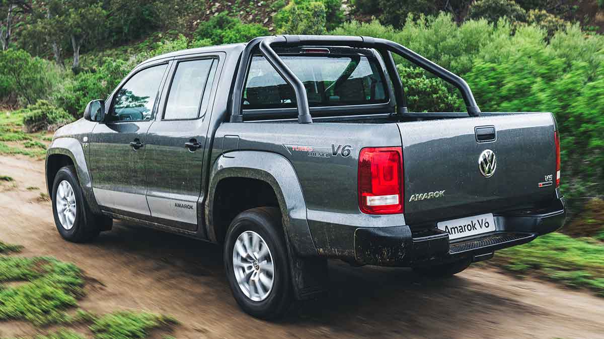 Rear side view of a grey Volkswagen Amarok V6 driving on a muddy, dirt road