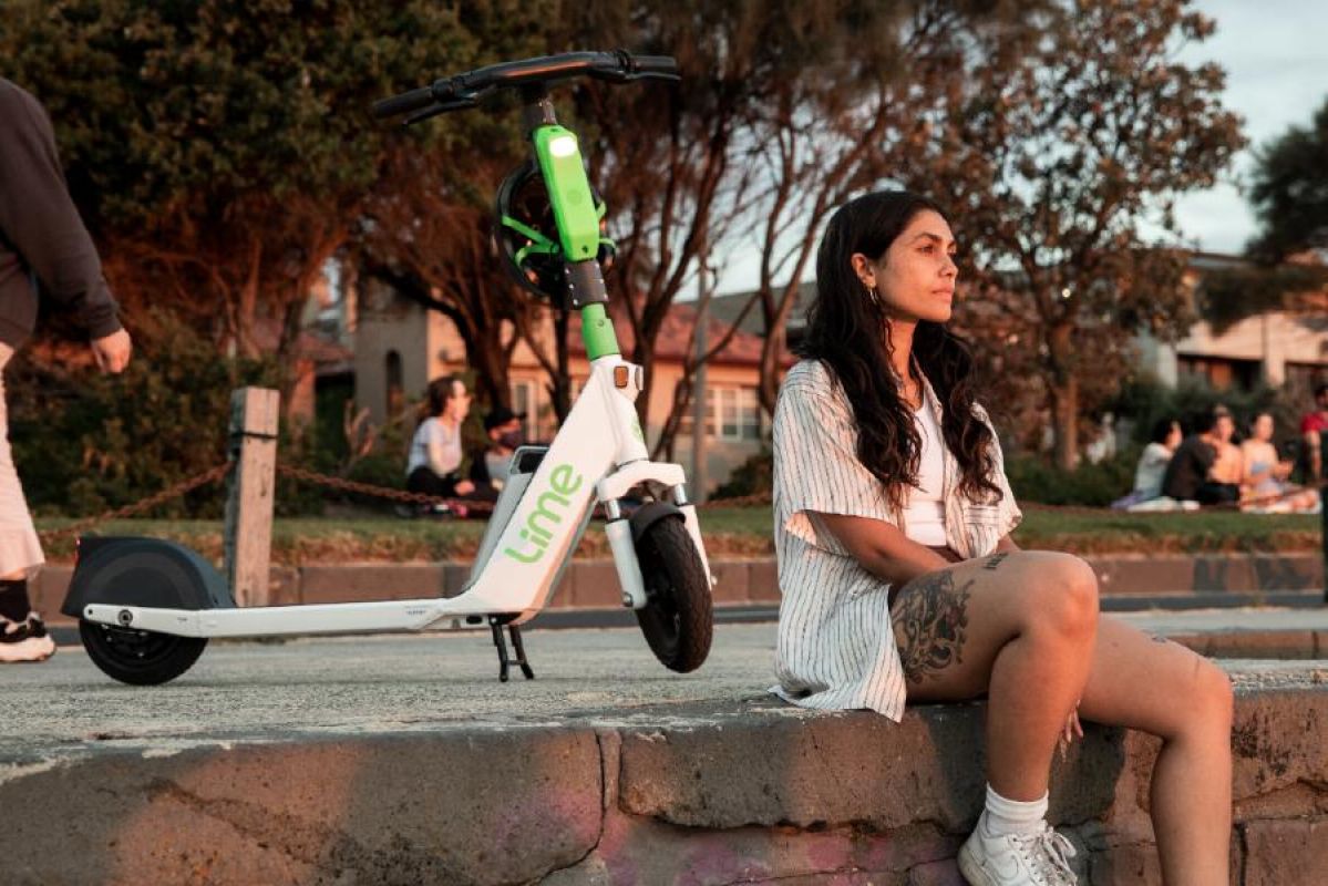 Woman sitting next to a Lime e-scooter at sunset