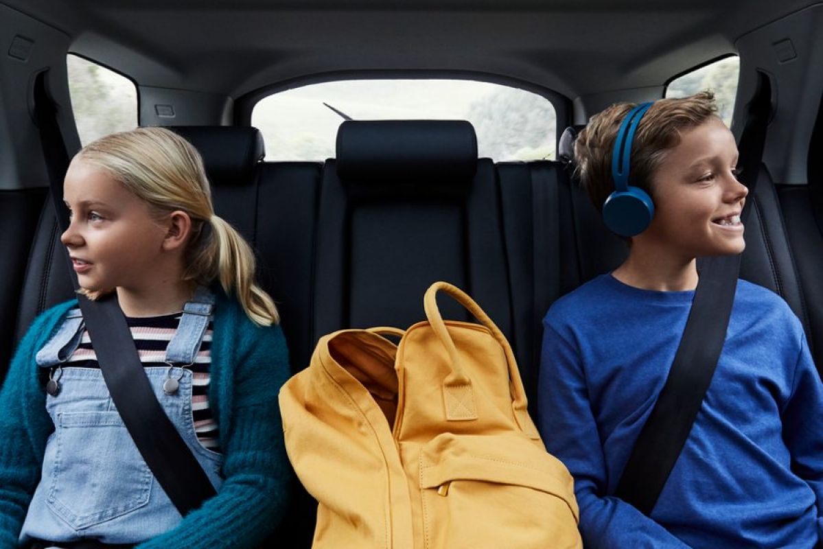 A boy and a girl sitting in the back seat of a car with a backpack between them