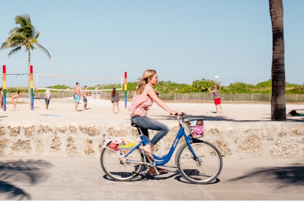 A woman cycling past people playing beach volleyball in Miami