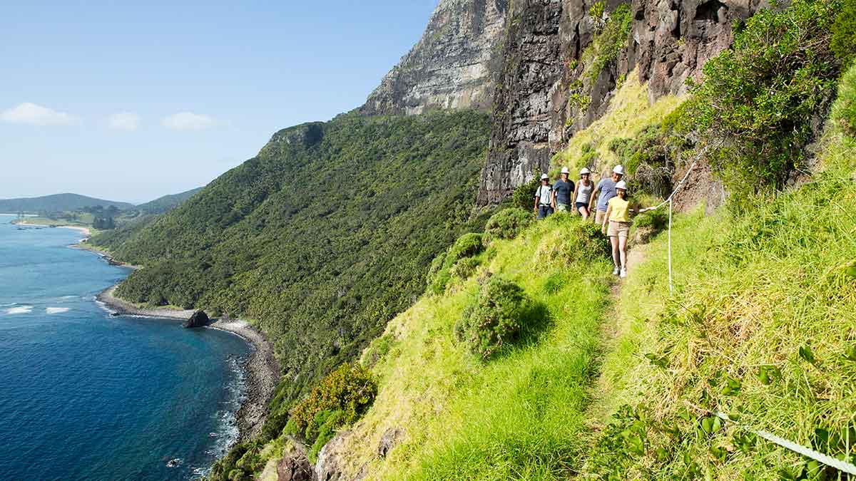 people walking along a cliff with water to the left