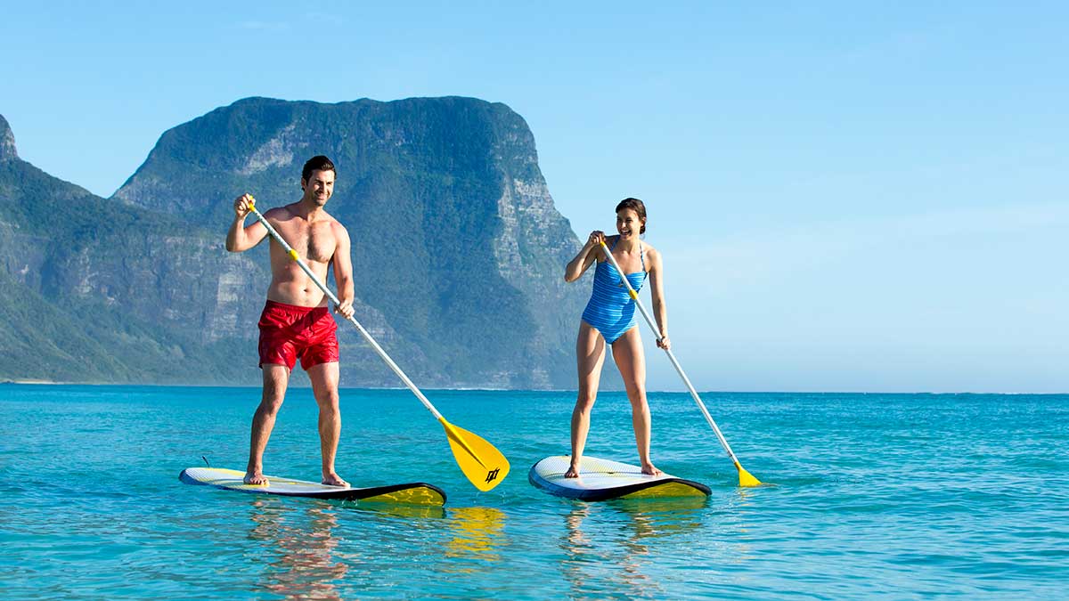 two people stand up paddle boarding in clear blue water