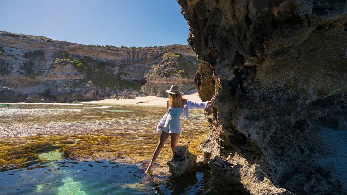 woman in a hat climbing over a rock pool