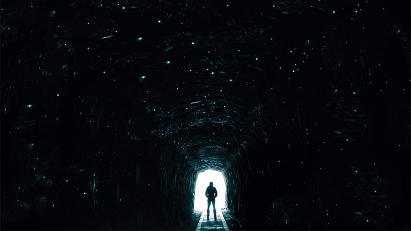 A person standing at the entrance to the Spray Tunnel which is dark but lit by glow worms