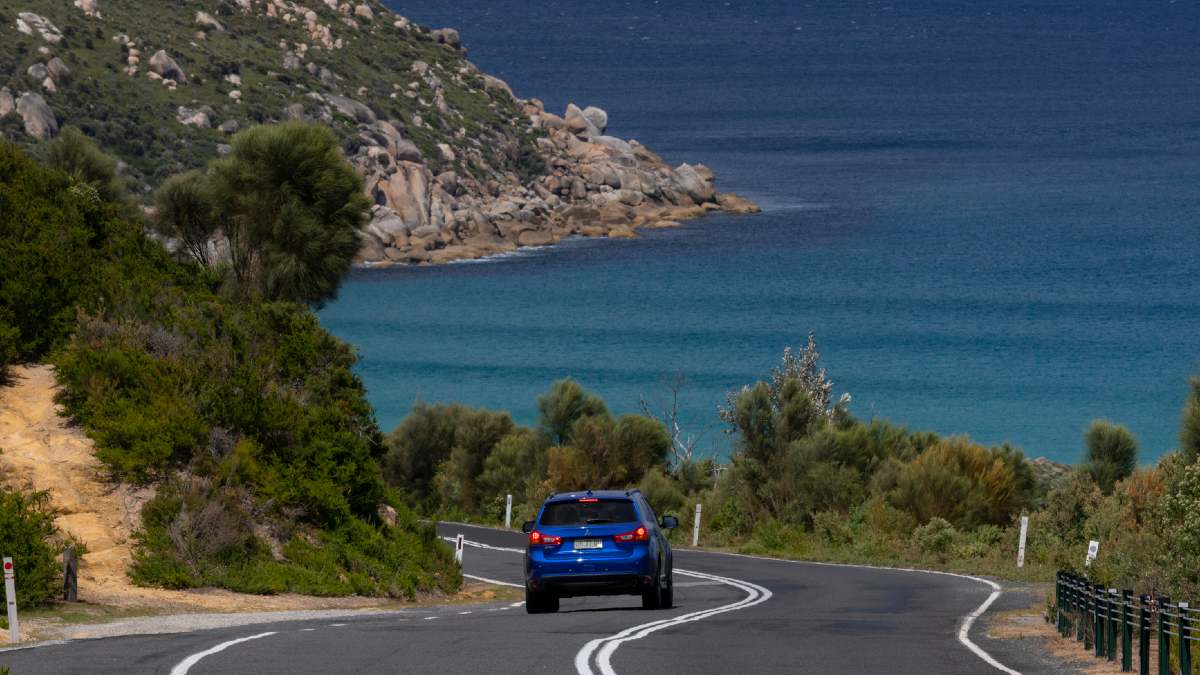 A blue SUV driving towards Wilsons Promontory with the ocean in the foreground