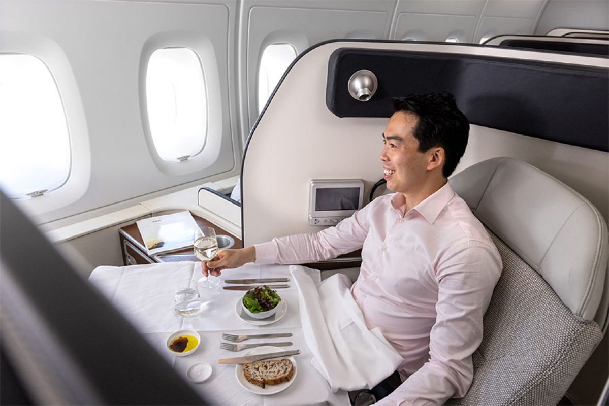 A man enjoying a glass of wine and a meal while smiling and sitting in a first class plane seat