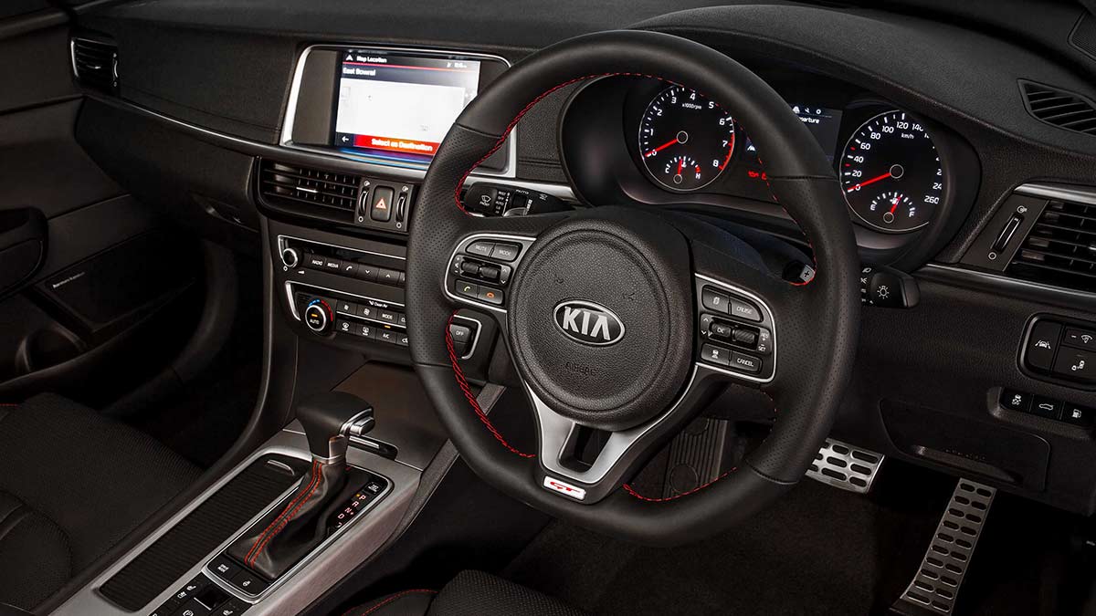 Black interior of the Kia Optima showing the centre console and steering wheel with red stitching