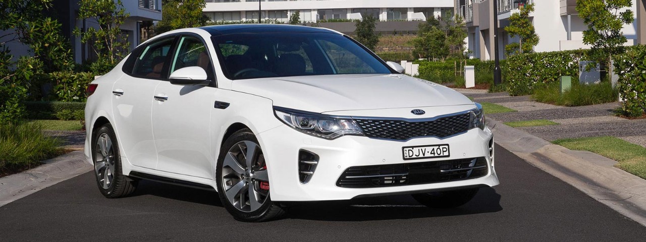 Front side view of a white Kia Optima car parked in a residential street