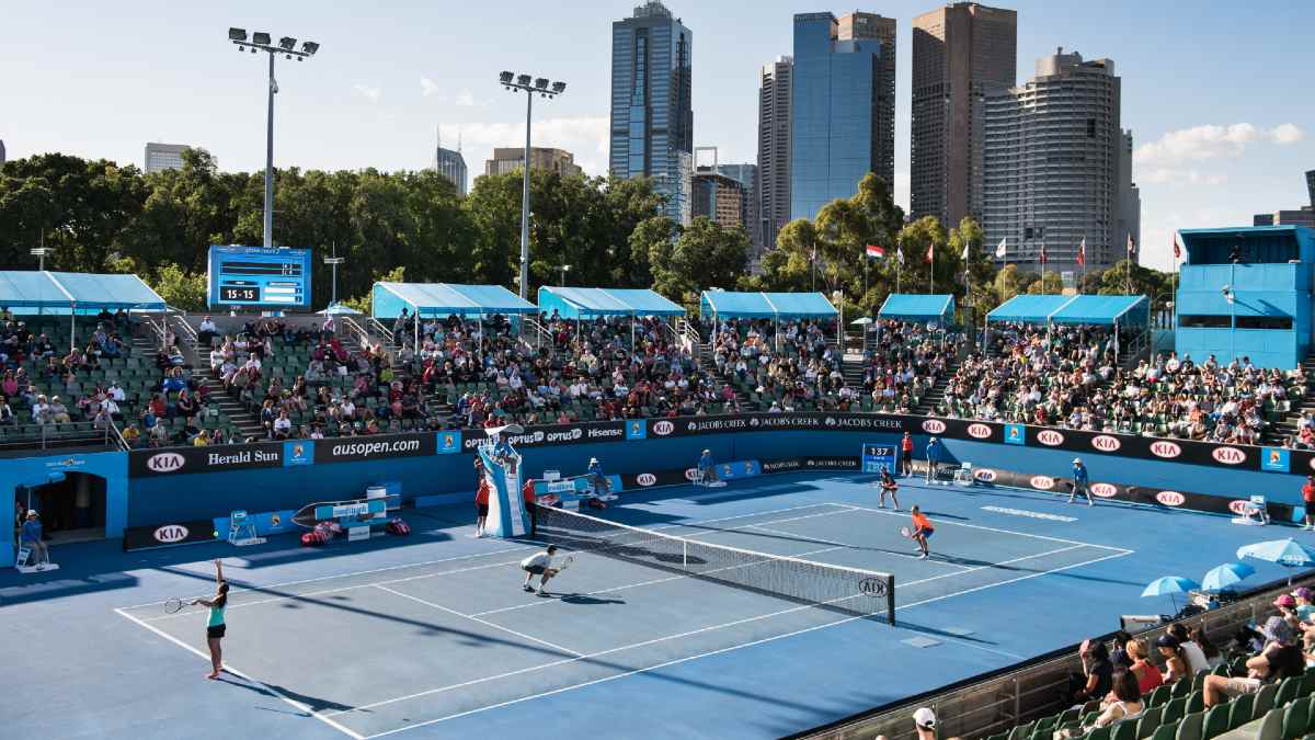 people playing tennis in front of a crowd with city skyline in background