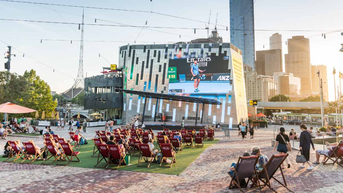 crowd watching tennis on Federation Square screen while sitting in outdoor lounge chairs