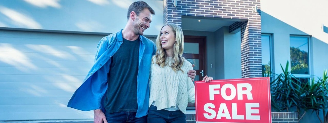 couple standing next to for sale sign outside home