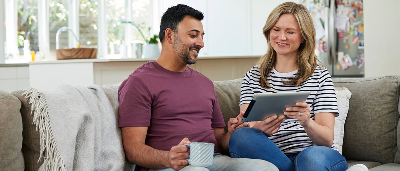 Home-contents-inventory-couple-couch-banner-RACV-1400x600 Man and woman on couch looking at tablet computer