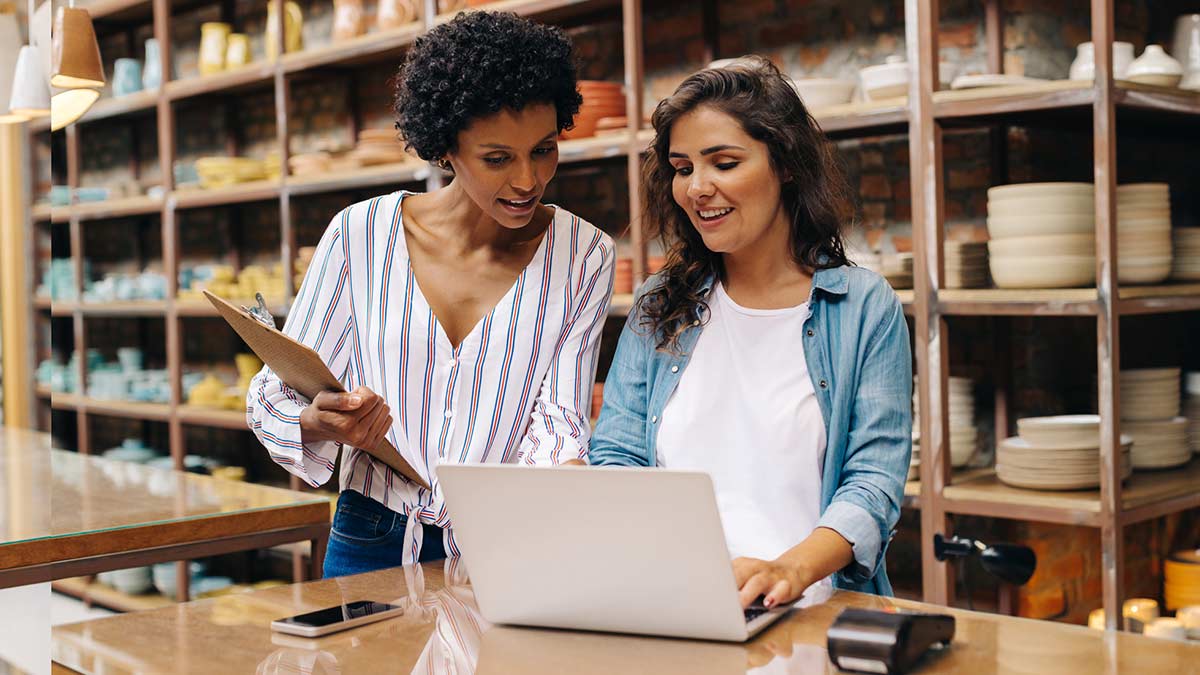 Two women business owners talking while looking at something on a laptop.