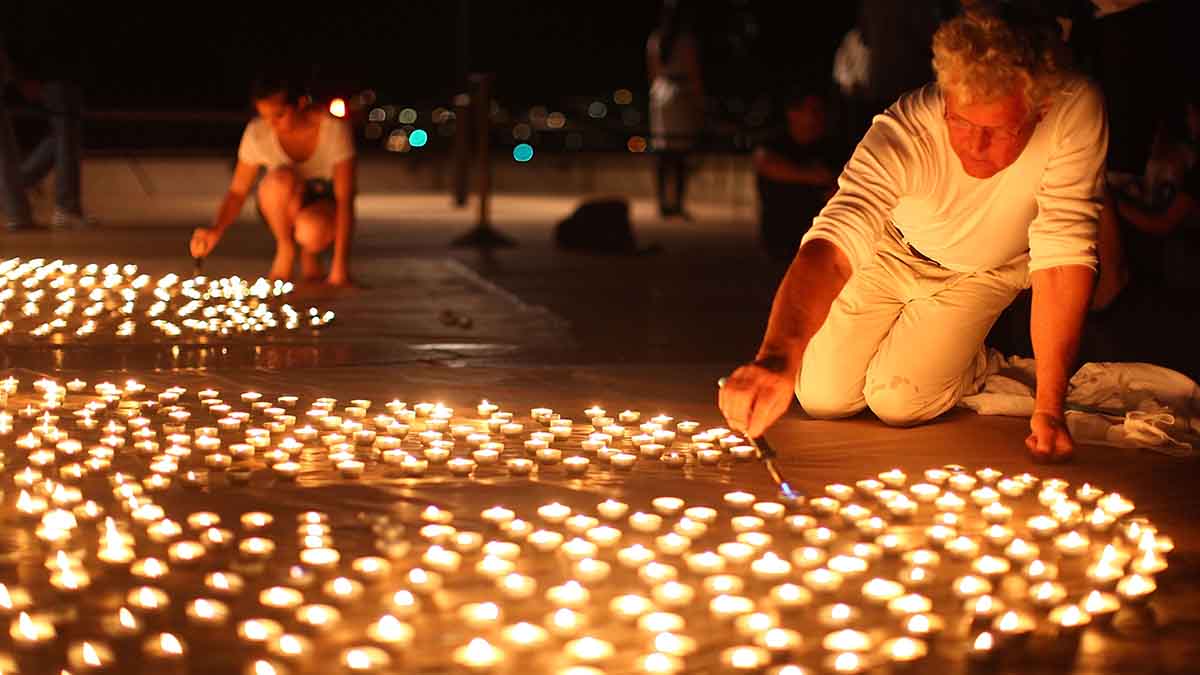 A man helps light a field of tea lights at nighttime for Earth Hour