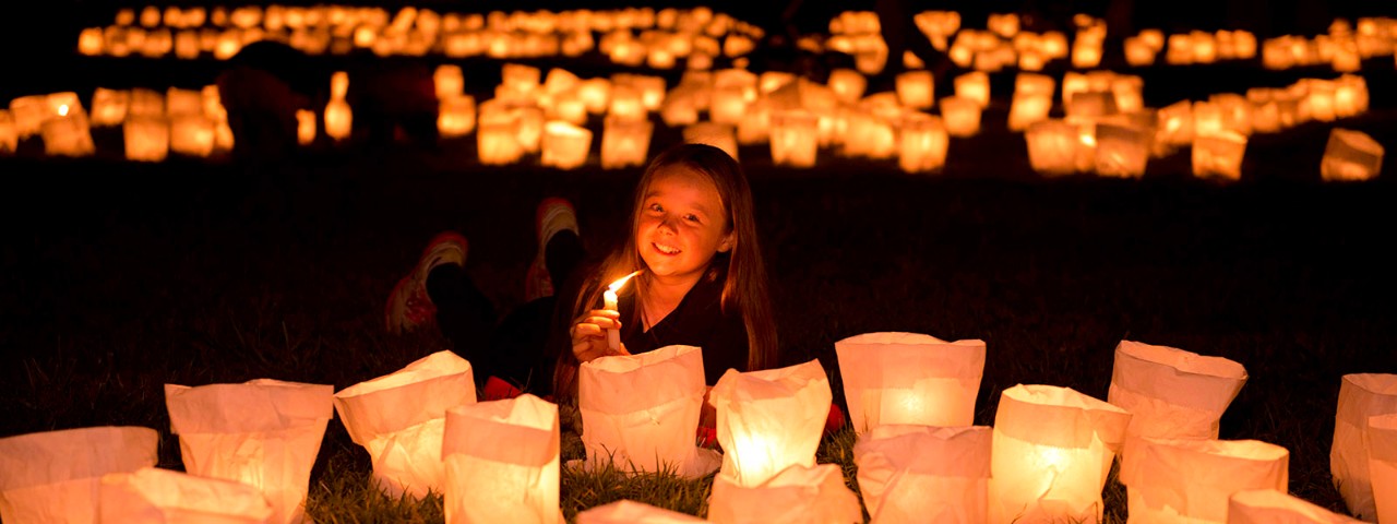 Earth Hour Night 2014 A young girl smiles while lying on a field at night. There are dozens of glowing paper lanterns in front and behind her.