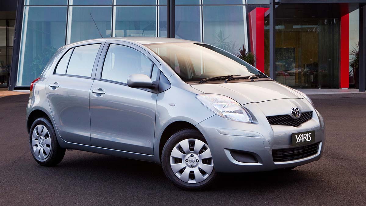 Front side view of a silver Toyota Paris parked in front of a glass building