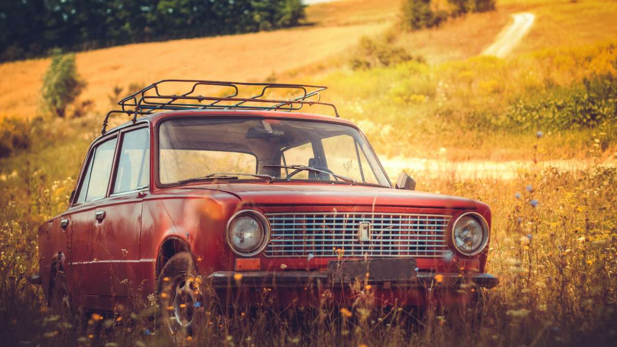 red car with roof racks parked in field next to road