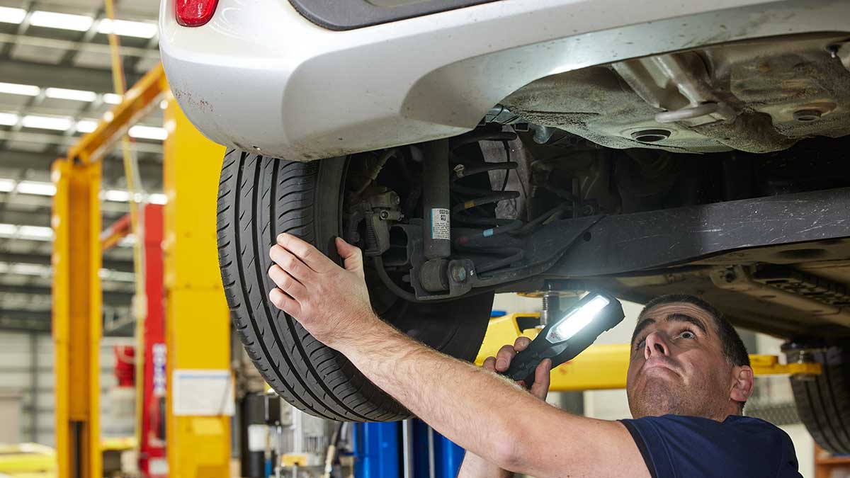 mechanic inspecting undercarriage of car