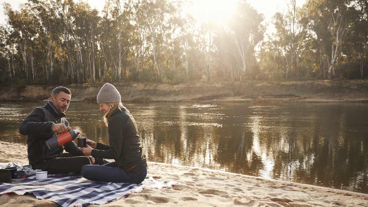 couple pouring tea on a picnic blanket in front of Murray River