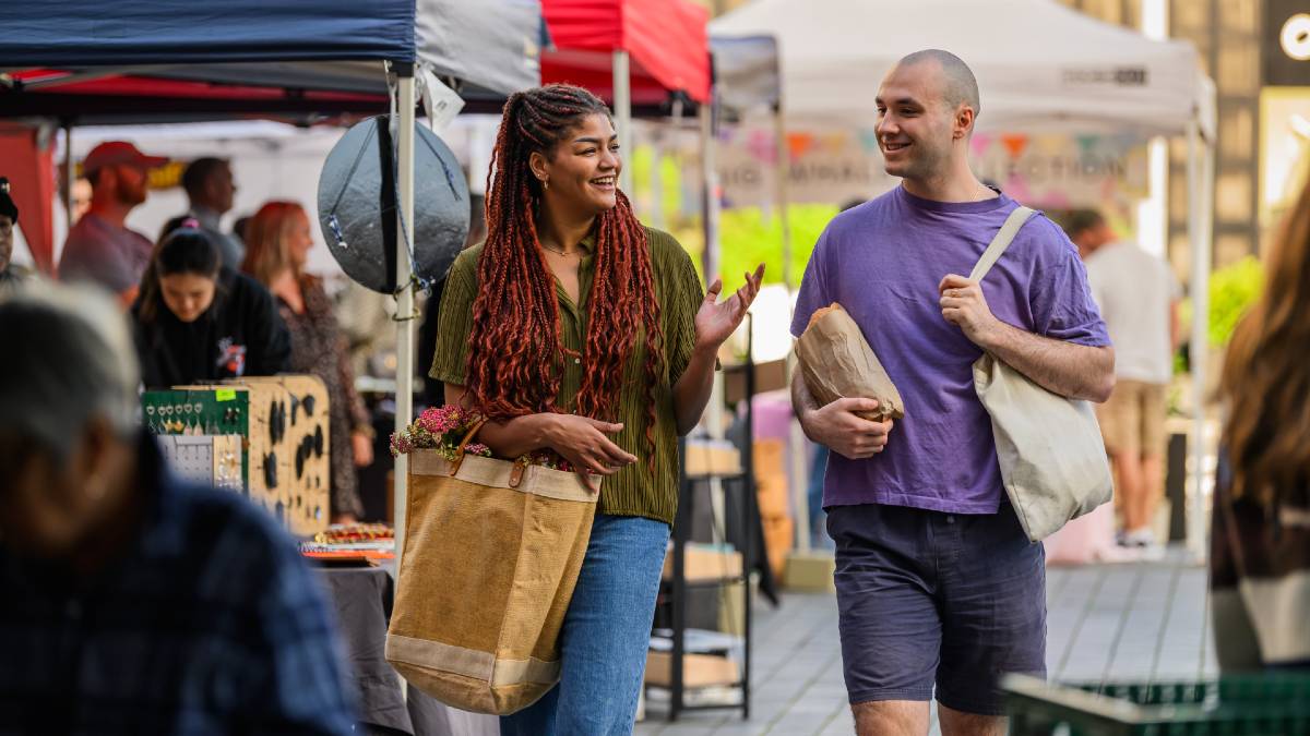 woman and man walking through outdoor market with groceries