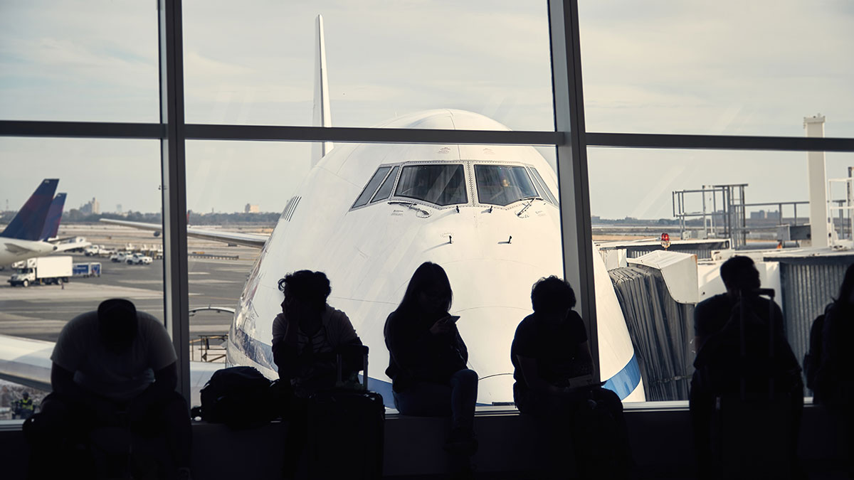 People at airport departure lounge at window with plane in background