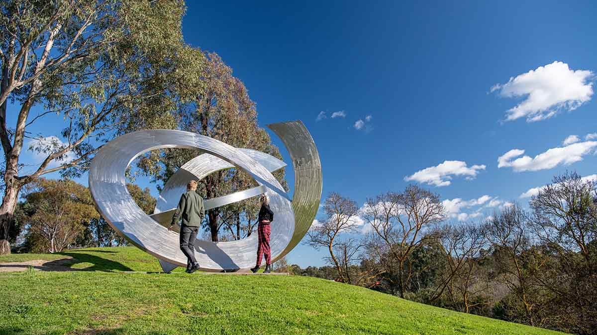 Man and woman looking at large circular outdoor sculpture in parkland at Heide museum